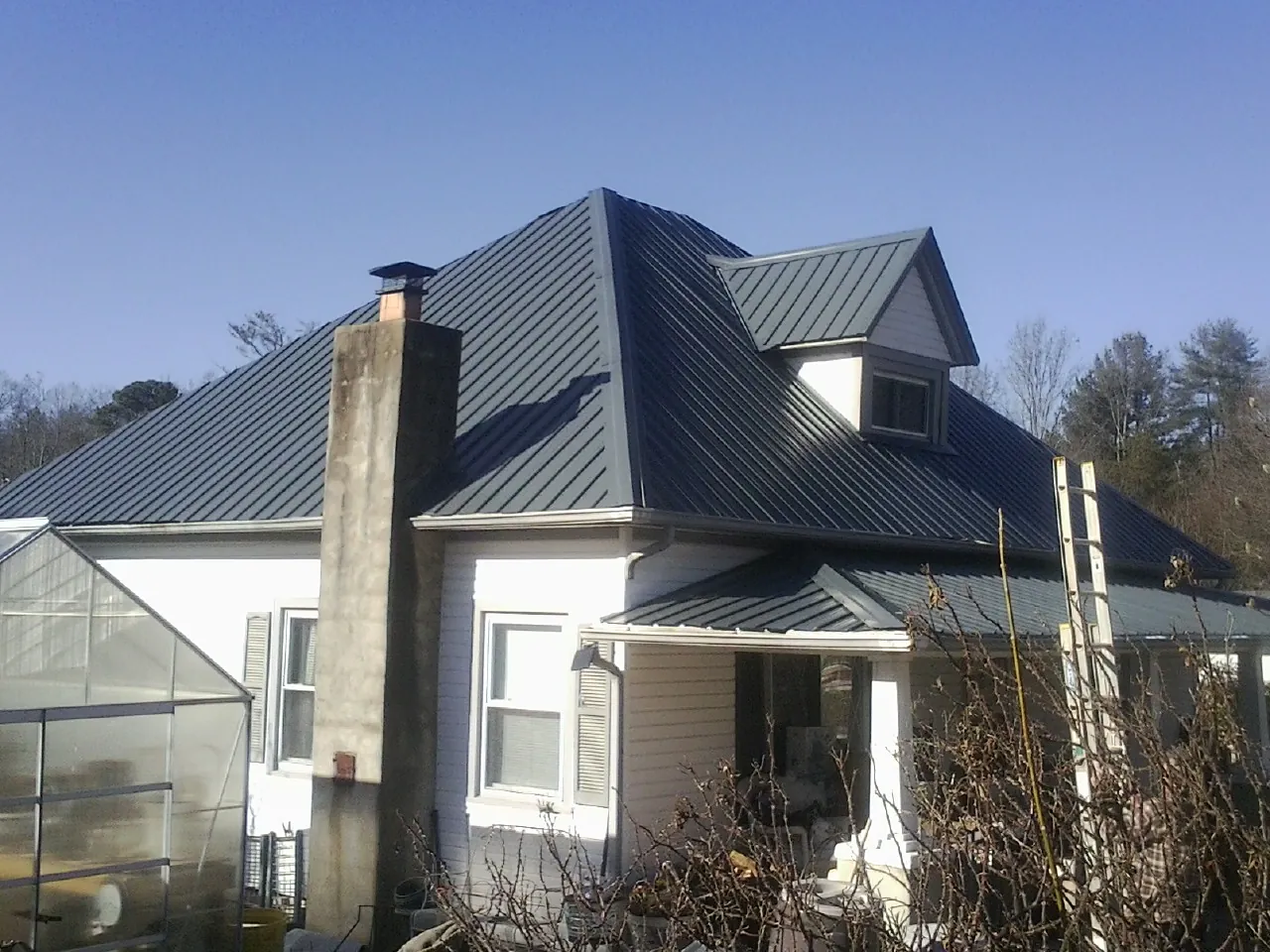 Dark blue standing seam metal roof on a white farmhouse with dormer — Slate & Tile Roof Repair by Roofing Brothers in Hartsville