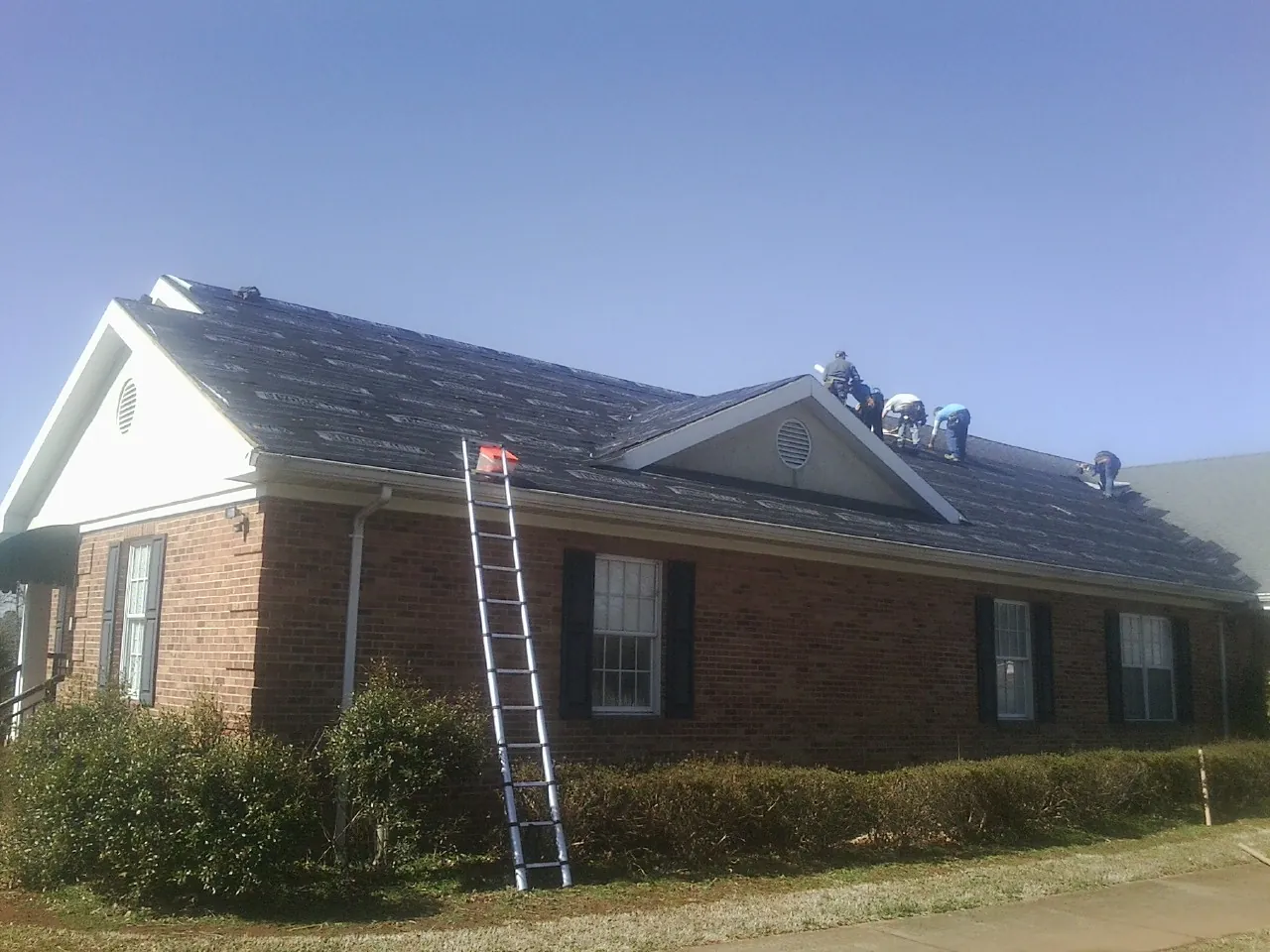 Crew tearing shingles off a brick ranch roof with a ladder set — Metal Roof Repair work by our crew in Hartsville
