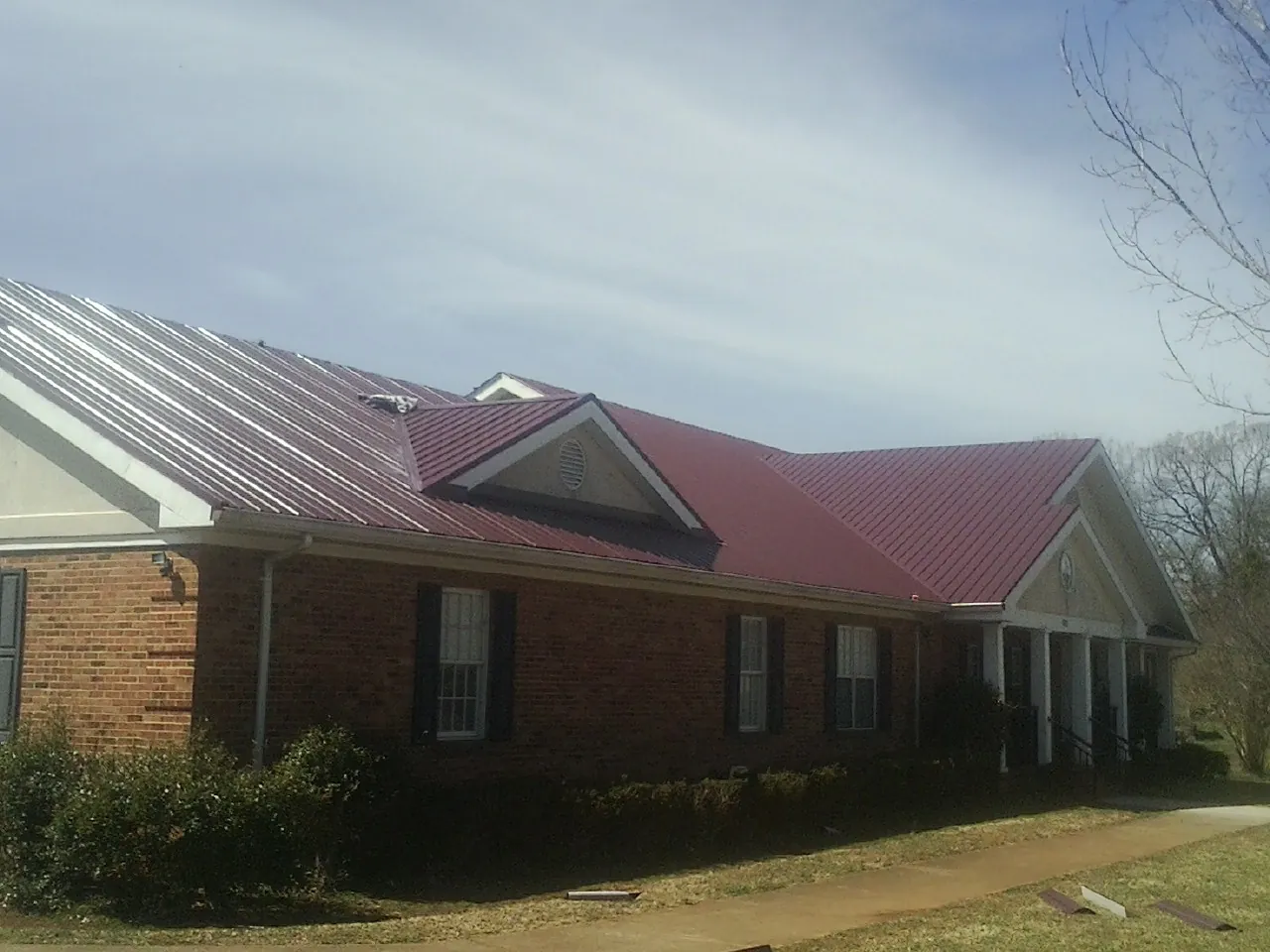 Red metal roof with gabled entries on a long brick building, from a Hail Damage Roof Repair job in Hartsville