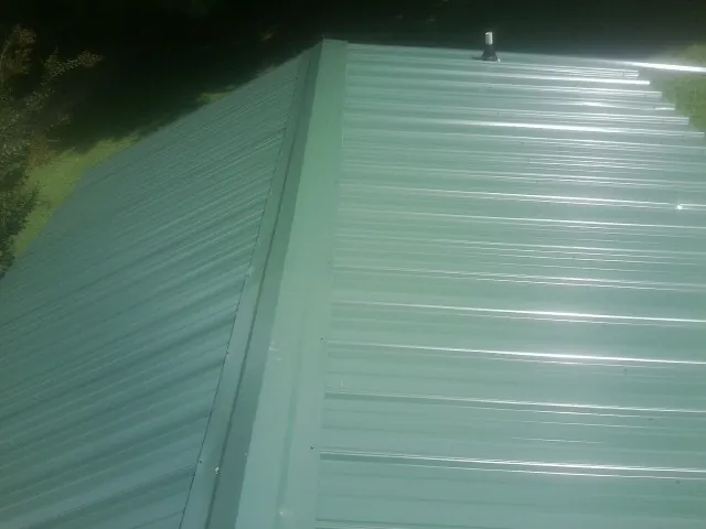 New green metal panels meeting at the ridge of a roof — Flat Roof Repair work by our crew in Hartsville