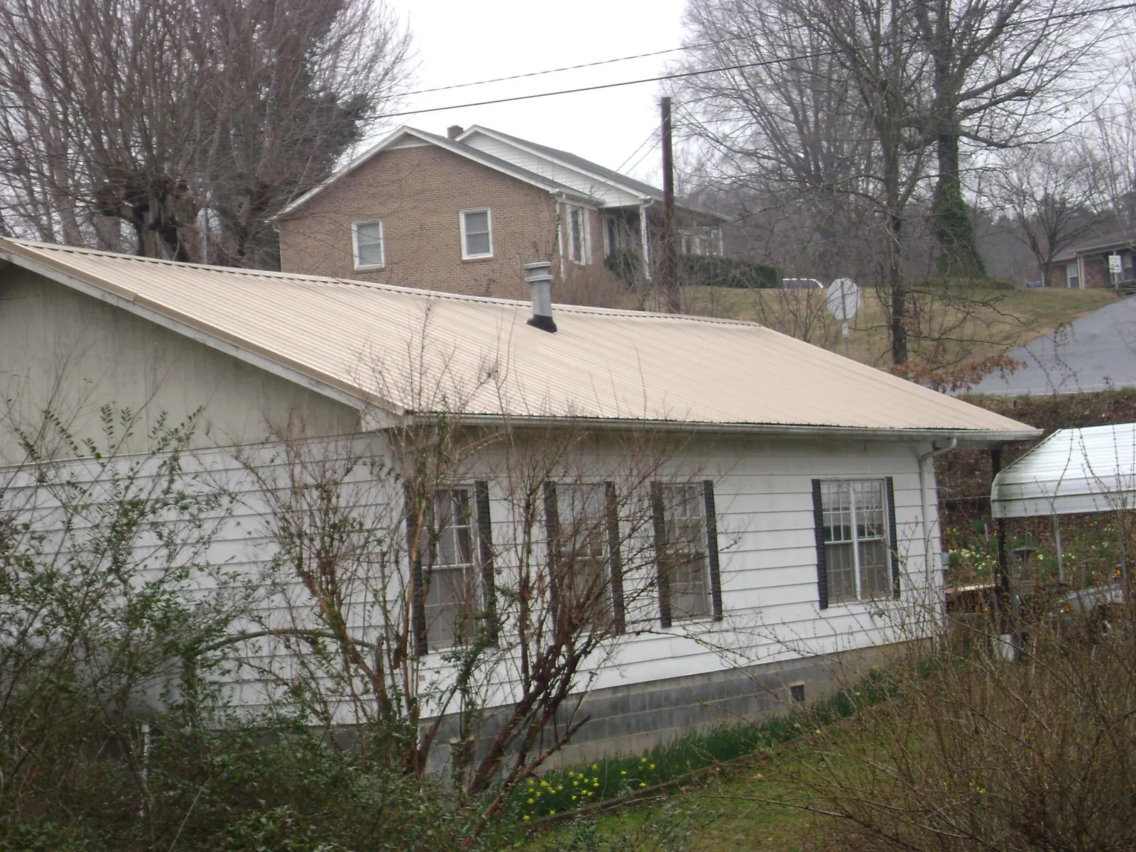 Tan metal roof on a white sided house set into a hillside — Commercial Roofing by Roofing Brothers in Hartsville
